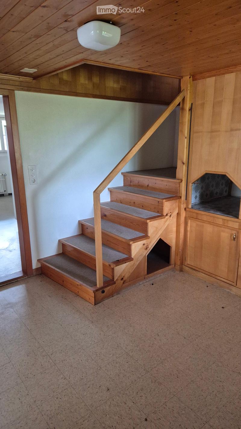 Wooden staircase with carpeted steps, wooden handrail, and built-in storage cabinet on the right side. The ceiling has exposed wooden beams and a single light fixture.
