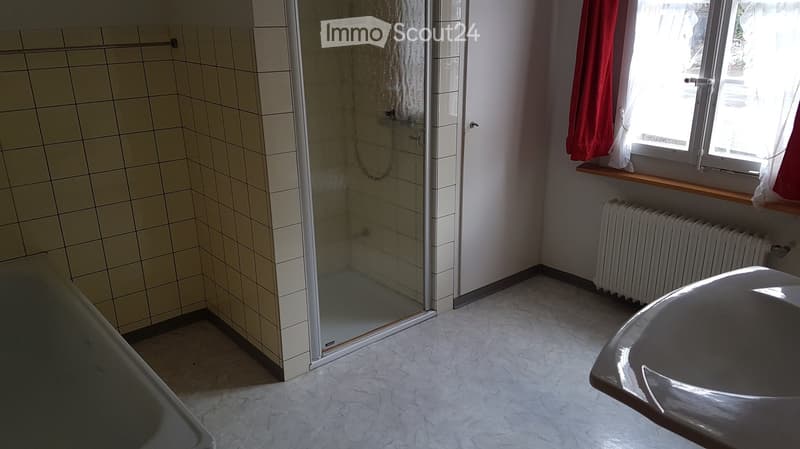 Bathroom with tiled walls, a glass-enclosed shower, a sink, a radiator, and a window with red curtains.