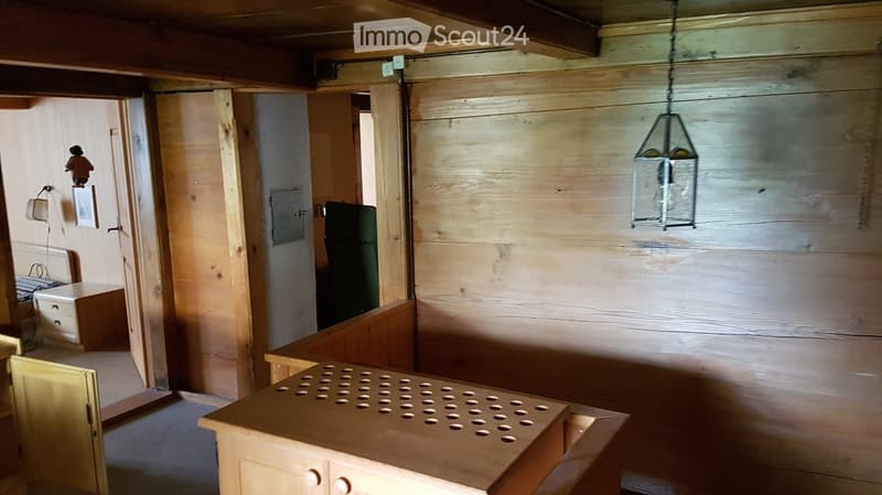 A rustic wooden room with a table, cabinet, hanging lantern, picture frame, and chair.
