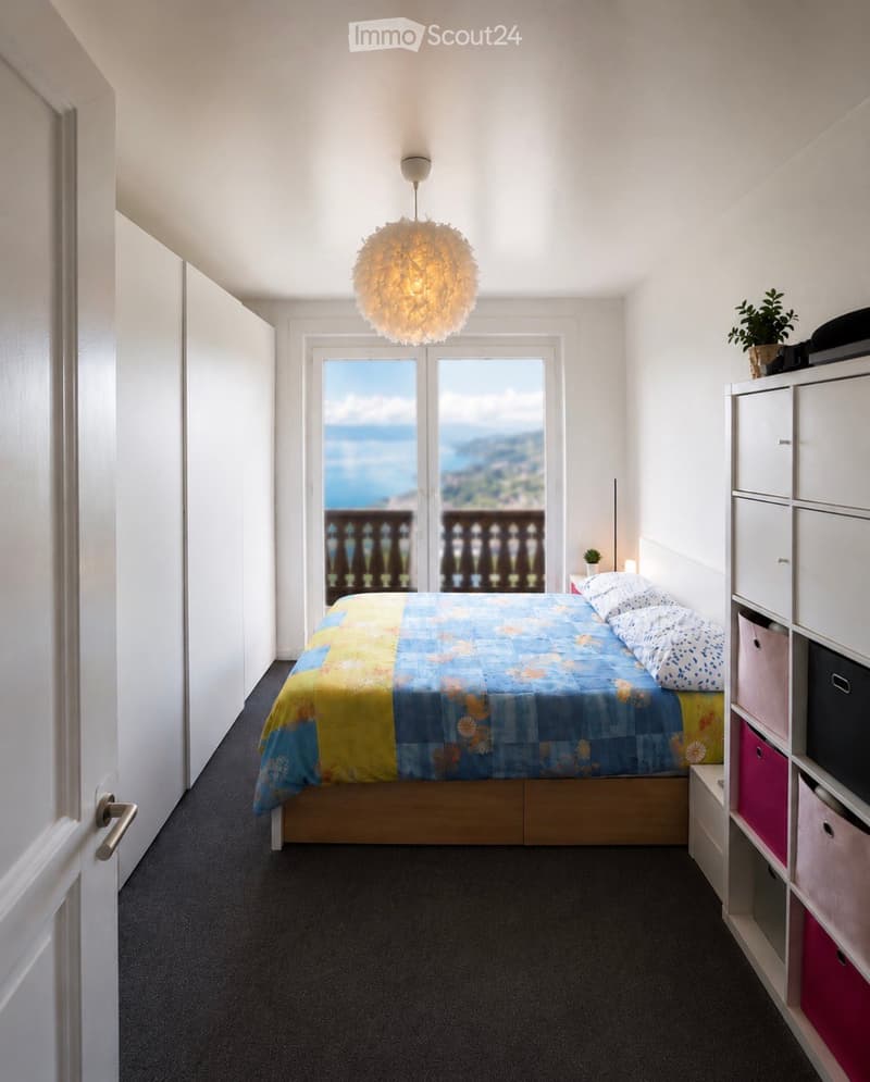 Cozy bedroom with a bed, colorful bedspread, pillows, a modern wardrobe with storage boxes, a hanging lamp, and a view of the sea through large windows.