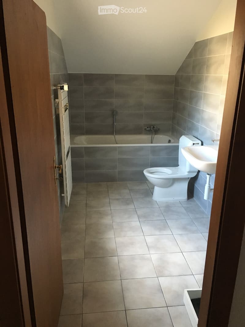 Modern bathroom with tiled walls and floor, featuring a toilet, sink, and bathtub.