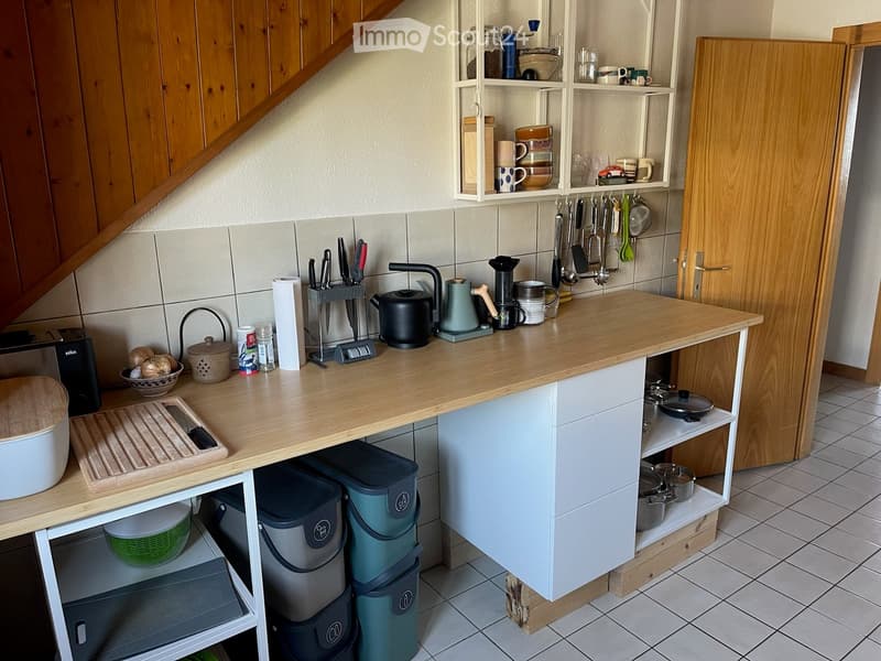 A modern kitchen with wooden countertops, white cabinets, and various appliances and utensils neatly arranged on the counter and shelves.