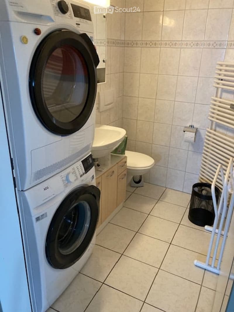 Bathroom with a washing machine and dryer stacked vertically, a toilet, a sink with a cabinet underneath, and a towel rack on the wall.