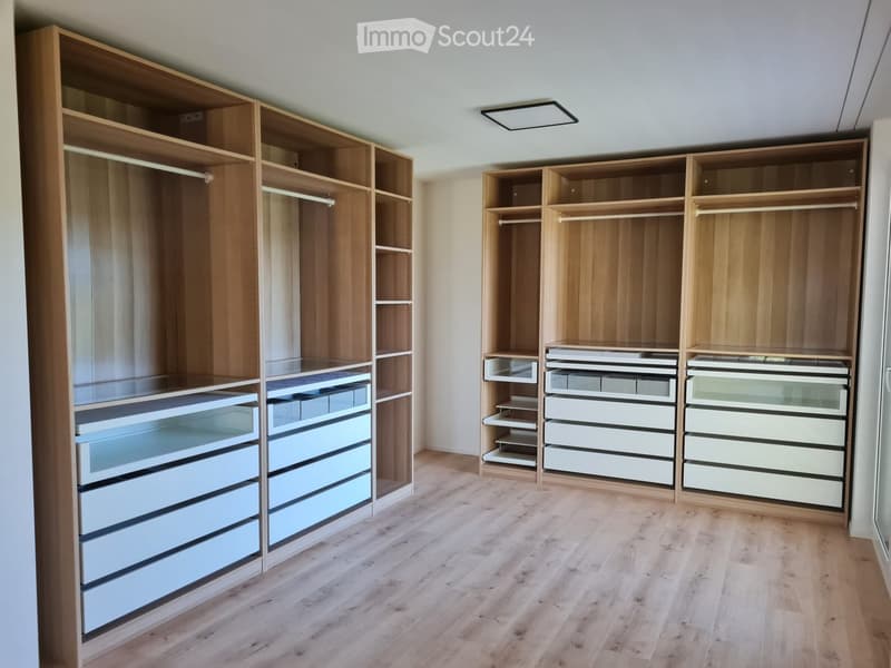 Empty room with wooden floor and built-in wooden wardrobes with shelves and drawers.