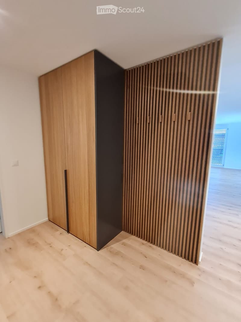 Empty room with light wooden flooring and modern wooden closet doors, featuring a sleek black panel design.