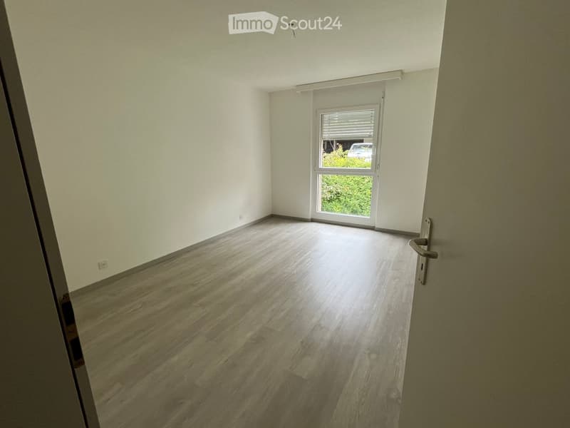Empty room with light wooden flooring, white walls, and a large window with blinds. No furniture or equipment is present.