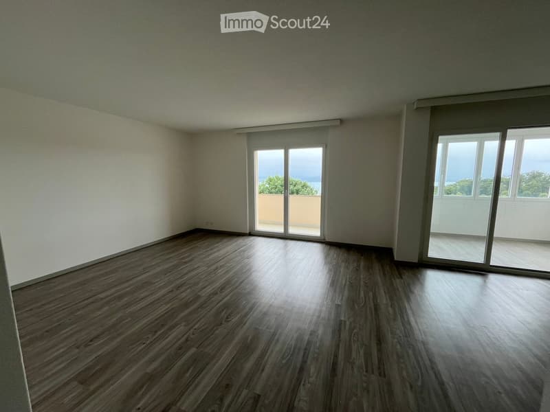 Empty room with wooden flooring, large windows, and sliding glass doors leading to a balcony.
