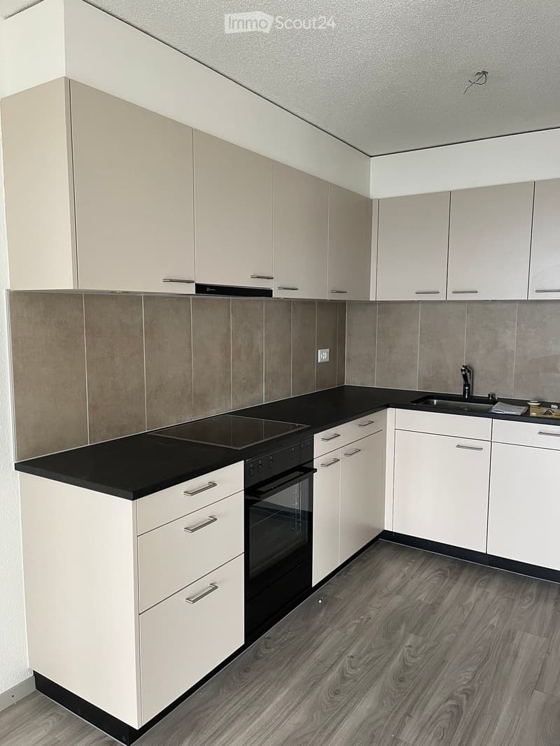 Modern kitchen with white cabinets, black countertops, and a built-in oven. Features a sink with a faucet and a sleek, contemporary design.