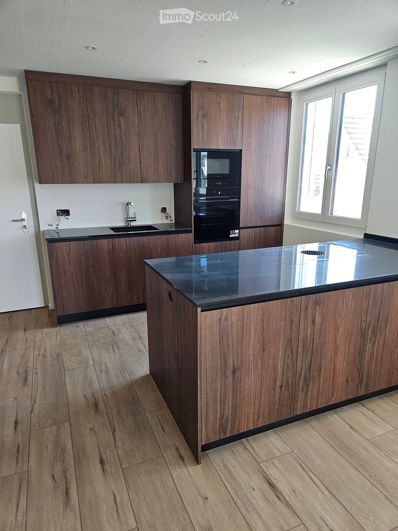 Modern kitchen with wooden cabinets, a central island with a black countertop, and built-in appliances including an oven and microwave.