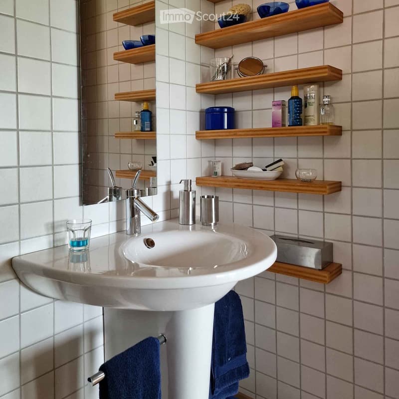 Modern bathroom with a white sink, chrome faucet, wooden shelves holding toiletries, and blue towels hanging on a rack.