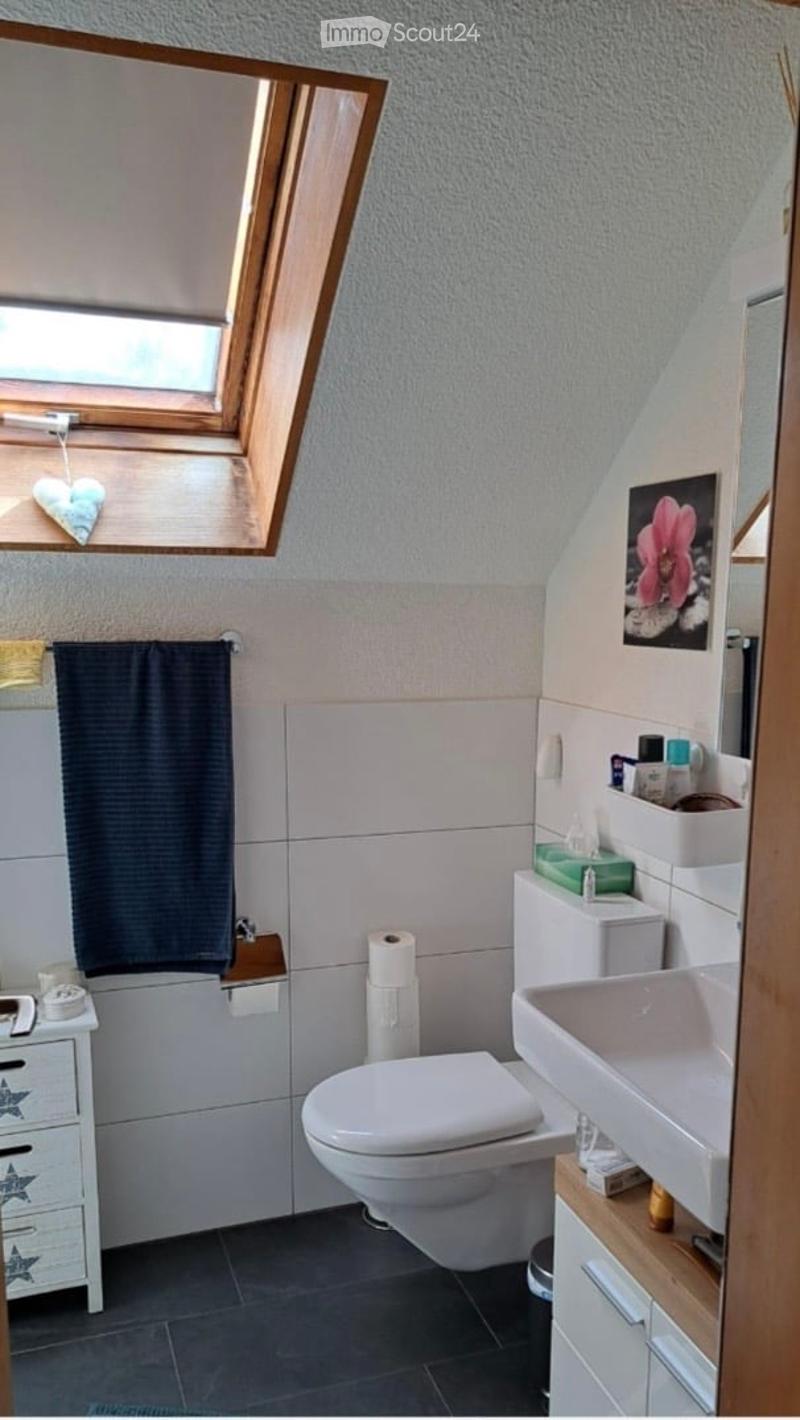 Bathroom with a toilet, sink, mirror, and a small cabinet. The room features a window with a dark curtain and a picture frame on the wall.