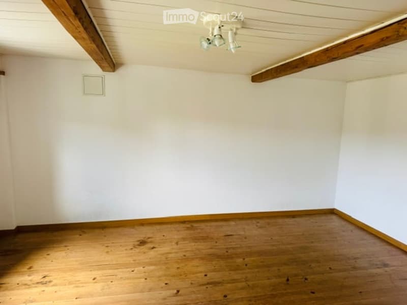 Completely empty room with white walls, wooden floor, and exposed wooden beams on the ceiling. No furniture or equipment.