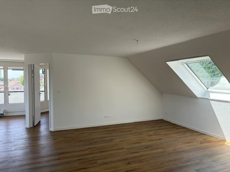 Completely empty room with wooden flooring, white walls, and large windows, including a skylight. No furniture or equipment.
