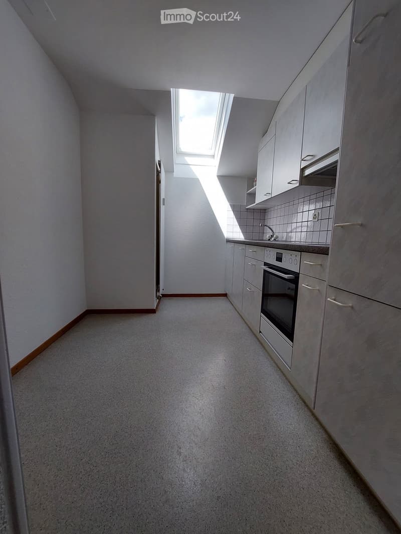 Empty kitchen with white cabinets, a built-in oven, and a small skylight window letting in natural light. The floor is carpeted, and the walls are painted white.