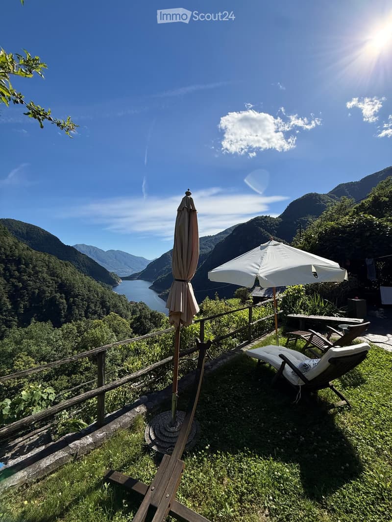 Balcony with wooden railing, lounge chairs, umbrella, and scenic mountain view.