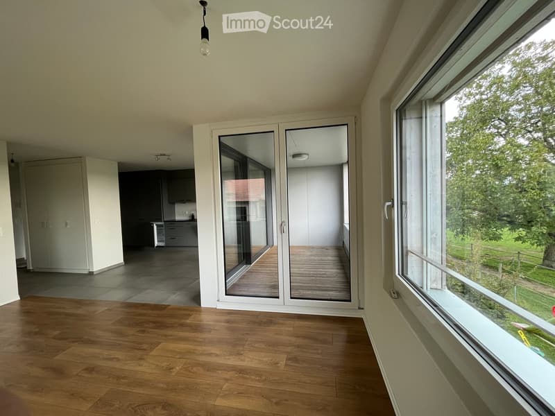 Empty room with wooden flooring, large windows, and sliding glass doors leading to a wooden deck area.