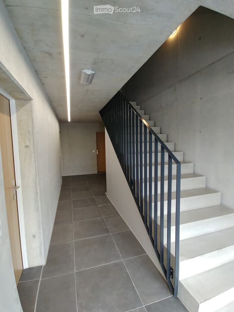 Modern hallway with tiled floor, white walls, and a staircase with a black metal railing leading upwards.