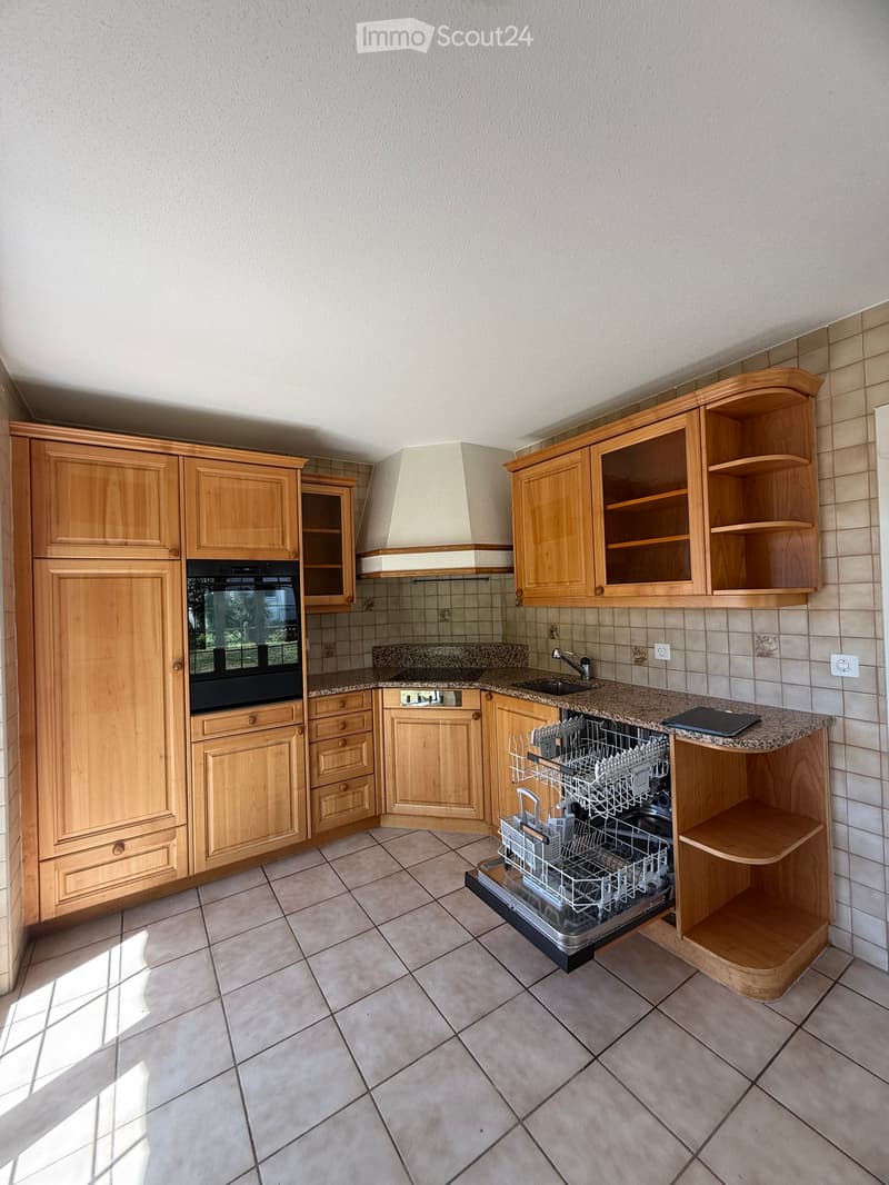 Well-lit kitchen with light wooden cabinets, granite countertop, built-in oven, dishwasher, and range hood.