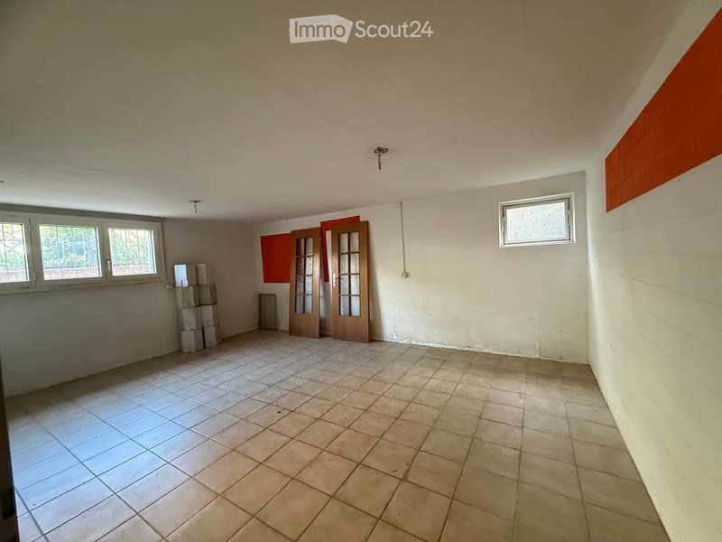Empty room with tiled floor, white walls, and two windows. There are two doors and a stack of boxes in the corner.