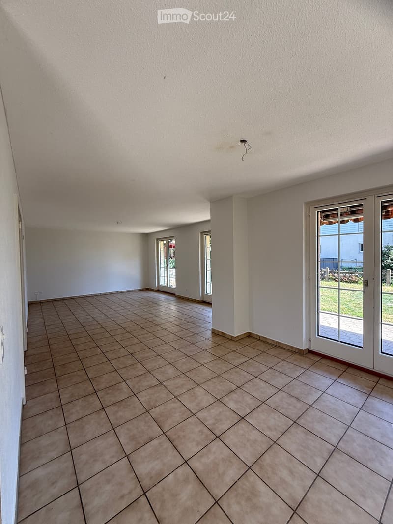 Empty room with tiled floor and white walls, featuring large glass doors leading to an outdoor area.