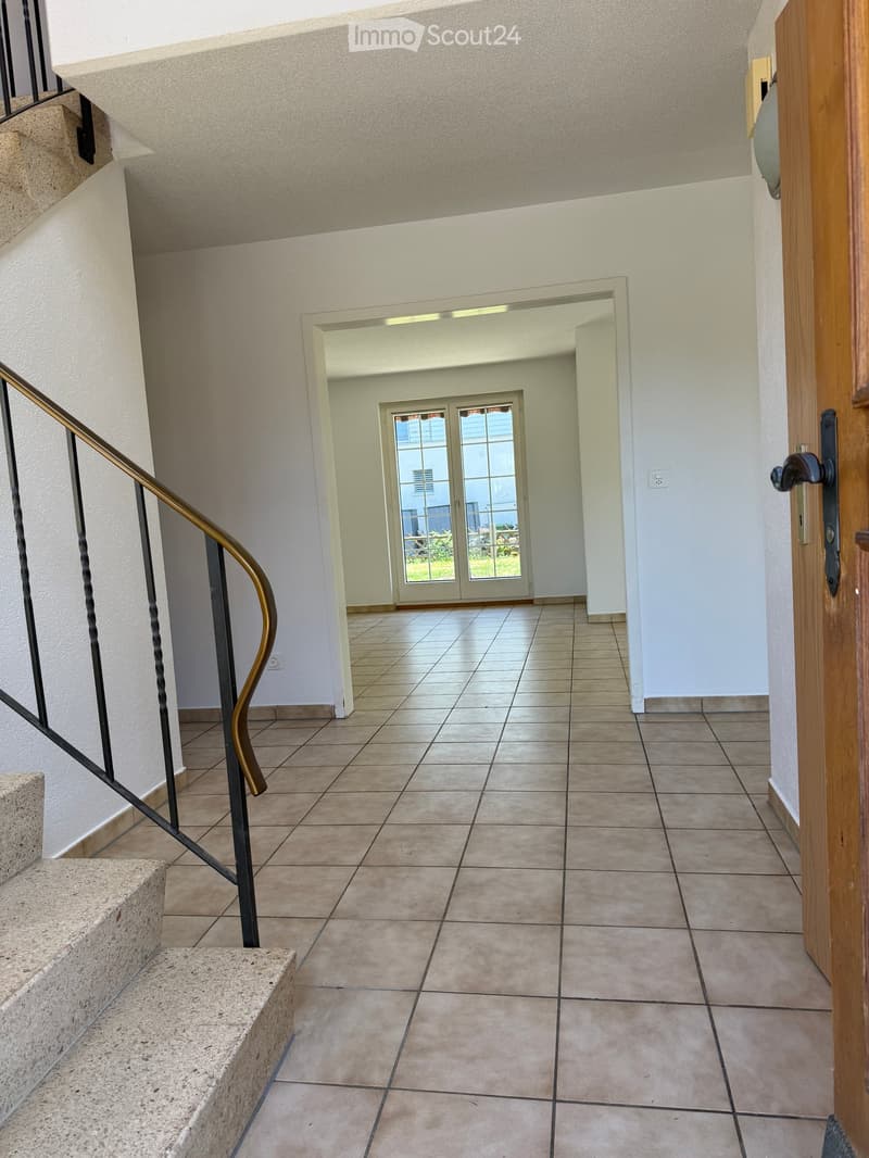 Empty hallway with tiled floor, white walls, staircase with metal railing, and a door leading to an outdoor area with glass doors.