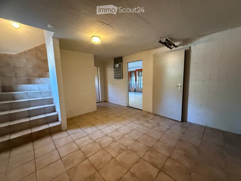 Empty hallway with tiled floor, staircase leading upwards, and a closed door on the right side.