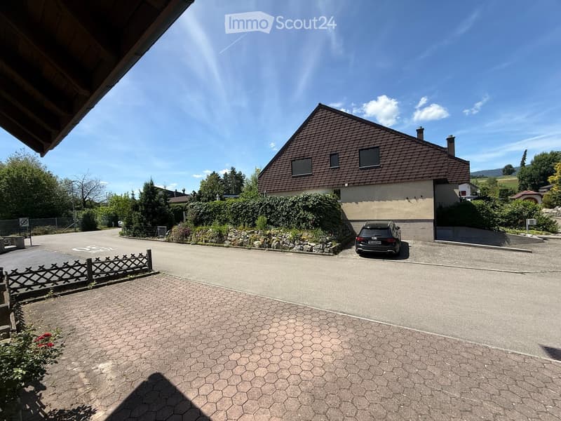 Two-story house with a brown tiled roof, surrounded by greenery and a driveway with a parked car.