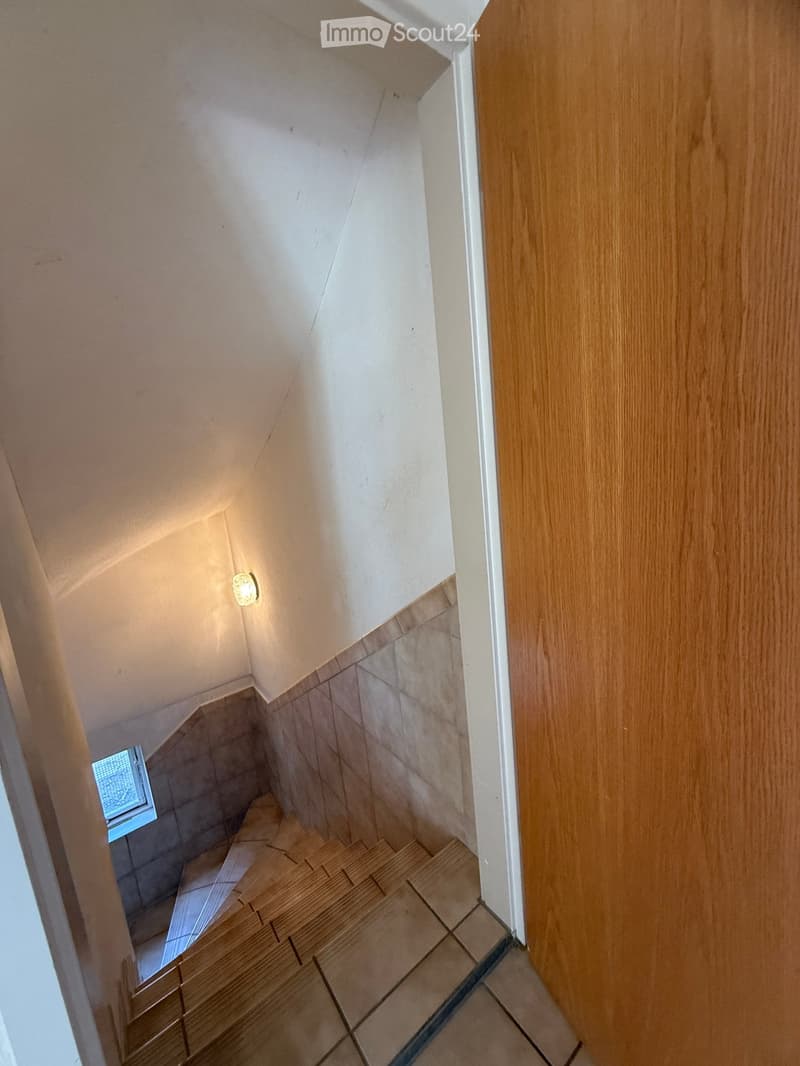 Wooden staircase with tiled walls and a small window at the bottom, illuminated by a wall-mounted light fixture.