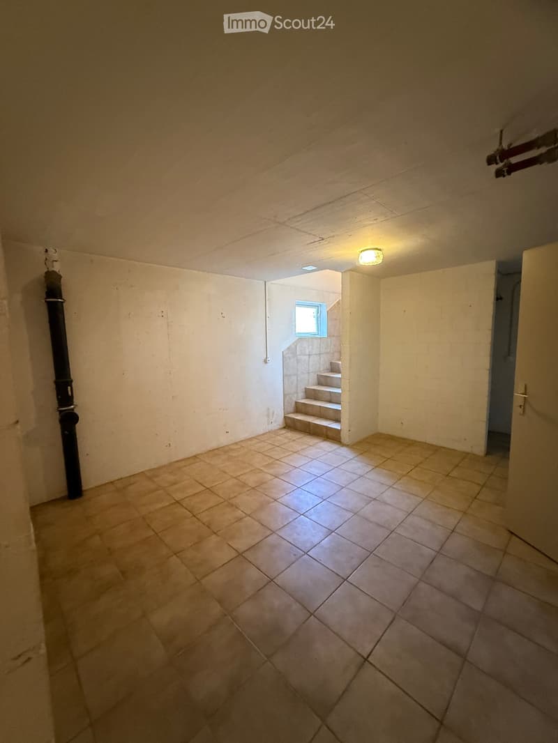 Empty room with tiled floor, white walls, and a small staircase leading to an upper level. There is a window at the top of the stairs and a door on the right side.