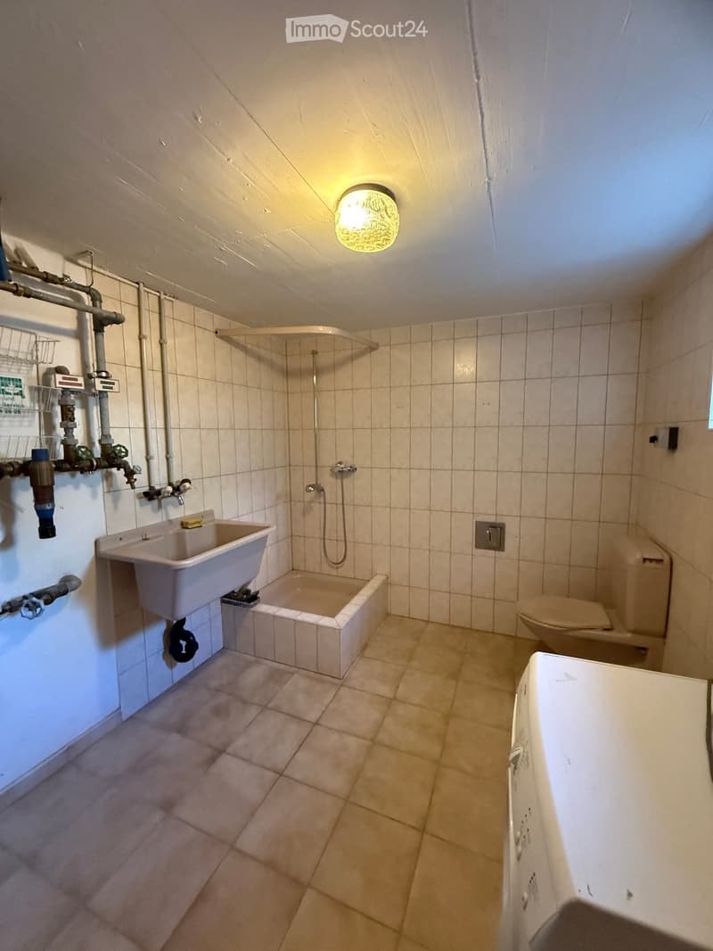 Bathroom with tiled walls and floor, featuring a sink, bathtub, toilet, and showerhead.