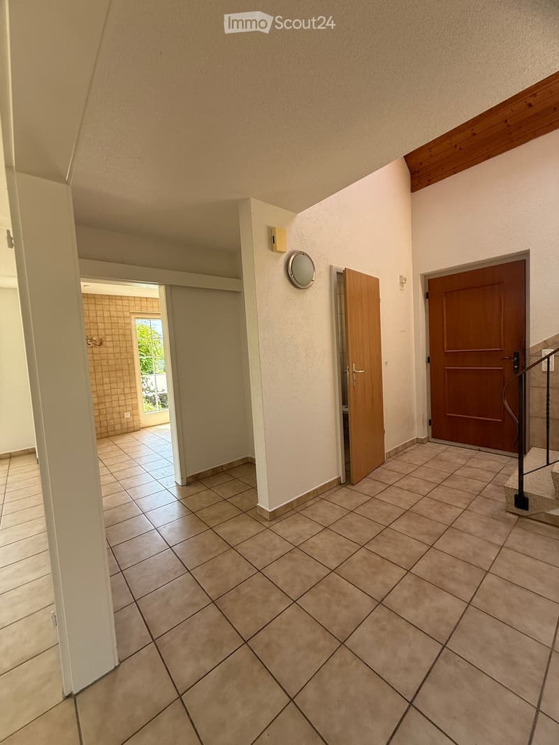 Empty hallway with tiled floor, white walls, and wooden doors leading to other rooms. A staircase is visible on the right side.