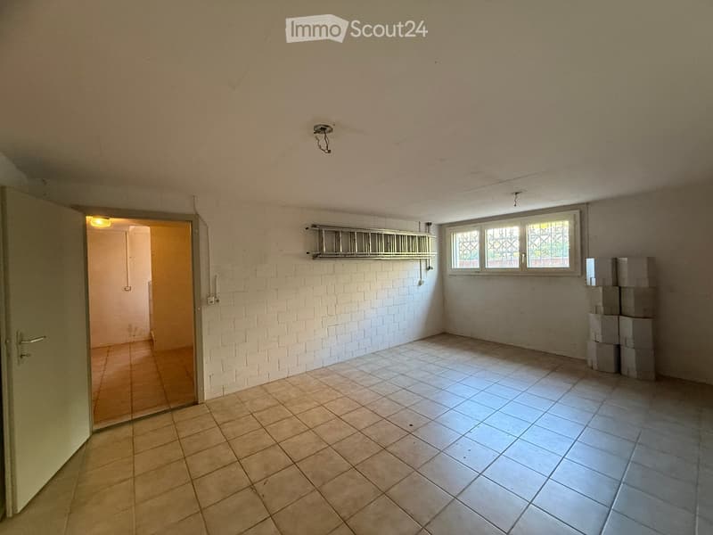 Empty room with tiled flooring, white brick wall, and a window with metal bars. A door leads to another room.