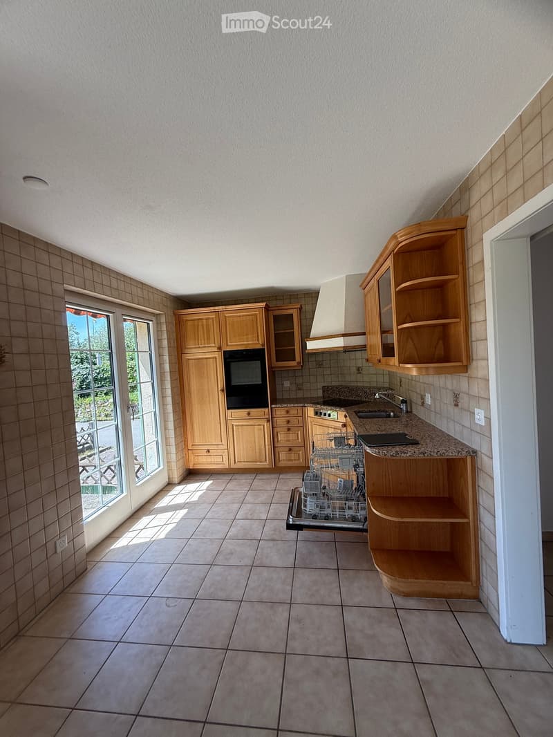 Bright kitchen with wooden cabinets, granite countertop, built-in oven, dishwasher, and sink. Large window provides natural light.