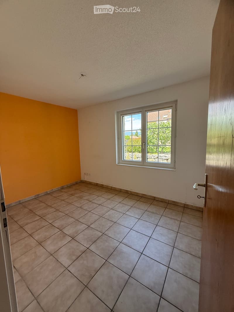 Empty room with tiled floor, beige walls, and a window with a view of greenery outside.