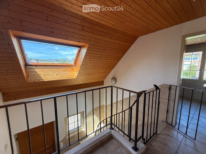 Staircase with wooden ceiling, skylight window, metal railing, and tiled floor leading to a room with a visible door and window.