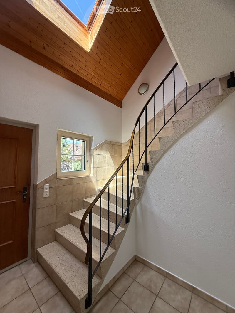 Staircase with wooden handrail, stone steps, and a skylight above, leading to a windowed area with a view of the outside.