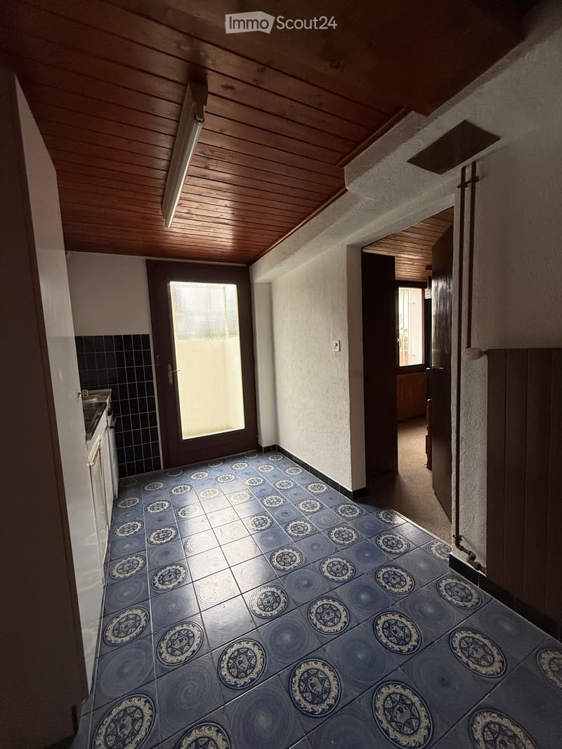 empty room with tiled floor, wooden ceiling, black tiled wall, door, entrance hall