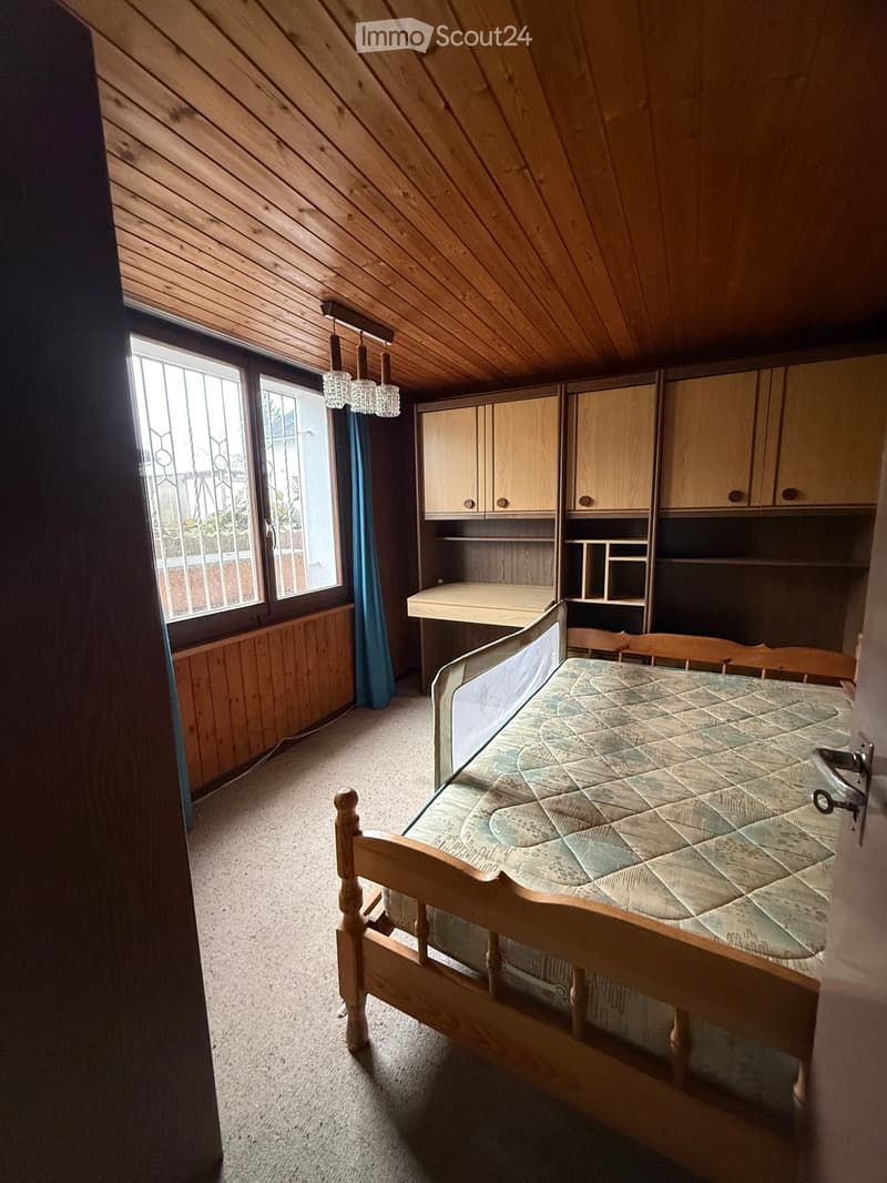 A room with wooden ceiling and flooring, single bed, wooden cabinets, desk, curtains, wooden bed frame