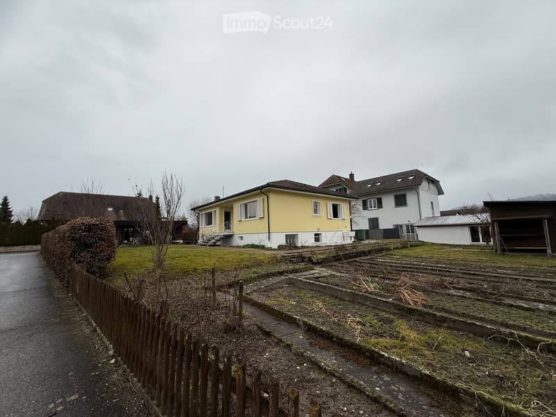 Yellow house, white windows, wooden stairs, brown roof, garden, other houses in the background