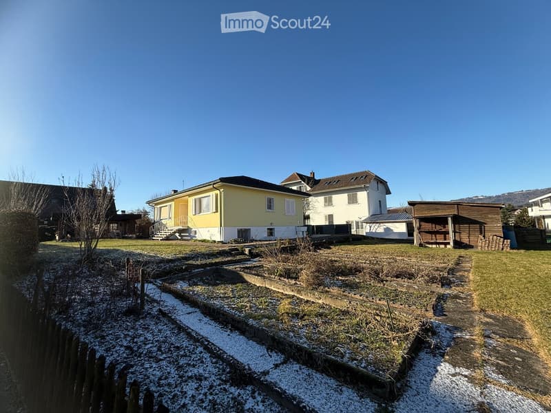 Two story house, yellow and white, chimney, garden with vegetable plots, and snow