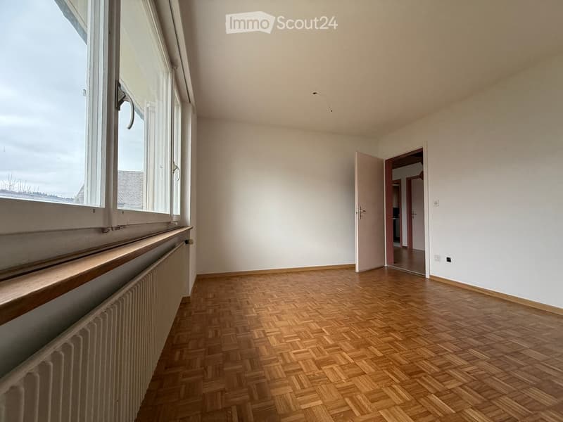 Empty room with wooden parquet flooring, large window, heater and two doors