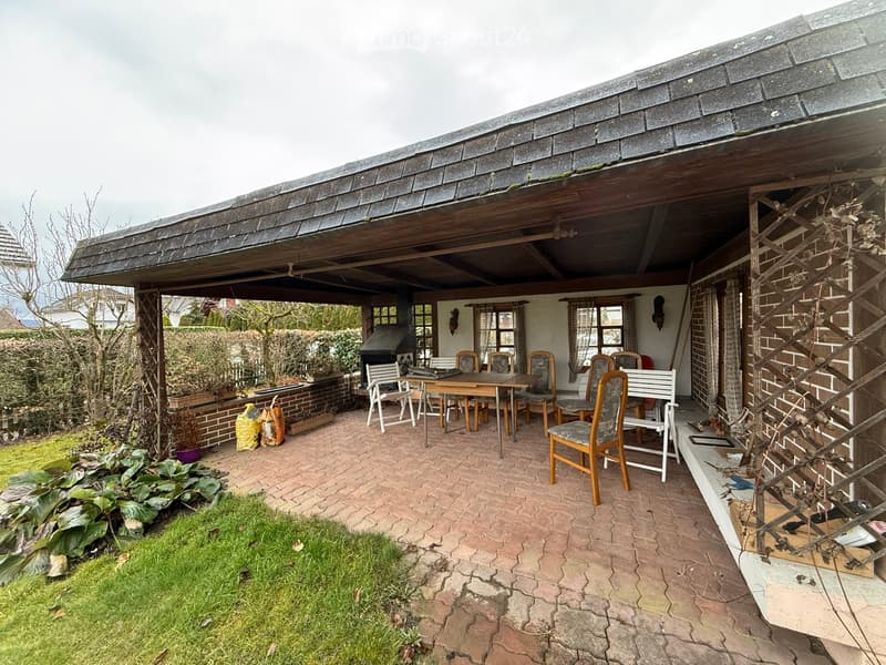 Outdoor seating with tables and chairs, brick paved floor, covered area with roof, plants, BBQ grill.