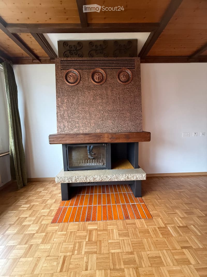 room with wooden floor, large fireplace, white walls, brown tiles around fireplace, electric outlet