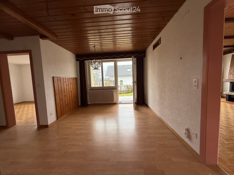 empty room with wooden floor, white walls, wooden paneling, chandelier, radiator, doors and windows, outside view