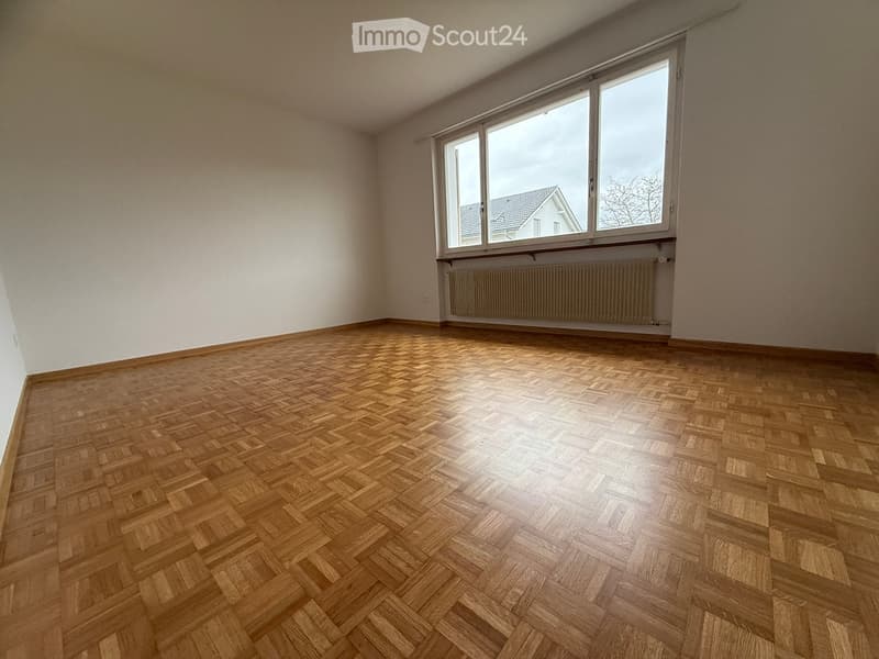 Empty room with wooden parquet flooring, white walls, large window, built-in radiator, view to outside