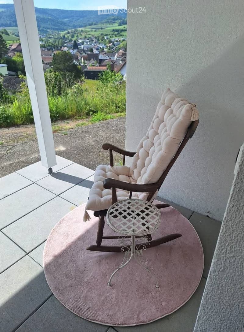 Balcony with a rocking chair, small table, and scenic countryside view.