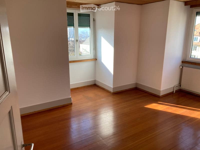 Empty room with wooden flooring, white walls, and large windows allowing natural light to enter.