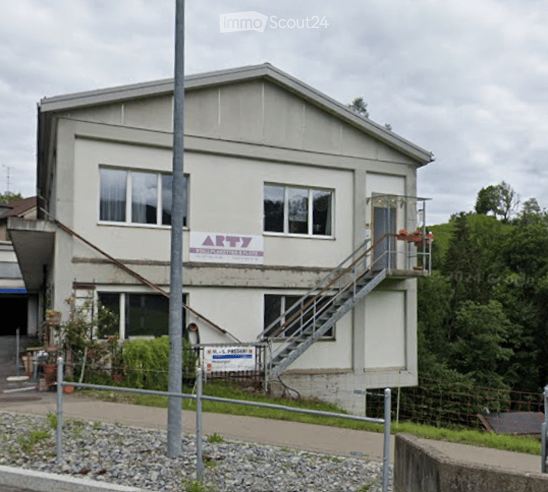 Two-story building with a flat roof, multiple windows, and a staircase leading to an upper entrance. The building has a sign that reads "ARTY" and appears to be a commercial or institutional structure.
