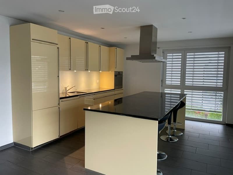 Modern kitchen with light-colored cabinets, stainless steel appliances, and a black countertop island with bar stools.