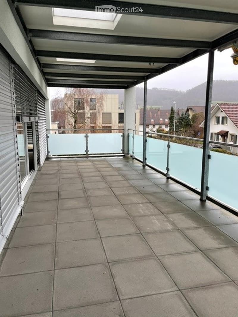 Balcony with tiled floor, glass railing, and a view of the surrounding area.